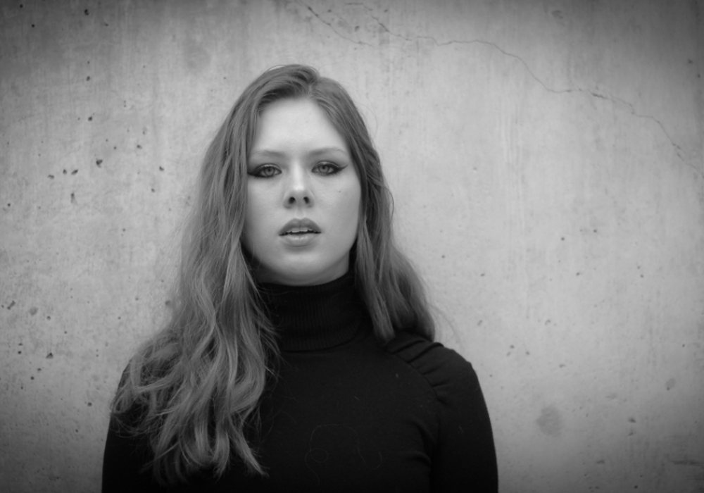 A black-and-white portrait of a woman against a concrete wall